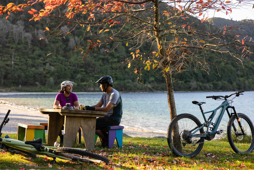 Couple resting at a picnic table by Lake Tikitapu with bikes.